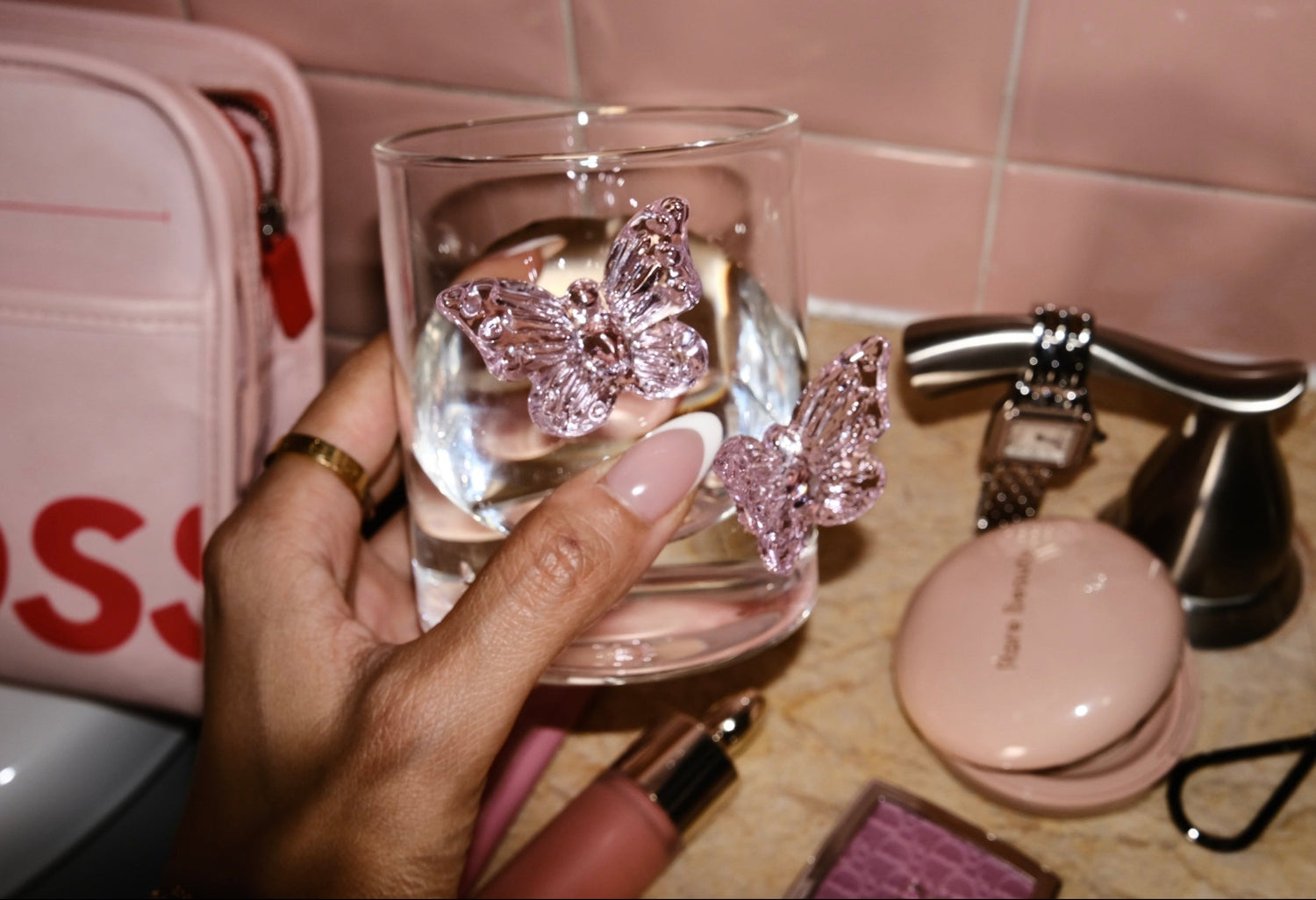 Glass with butterfly decorations held by a hand on a vanity table.